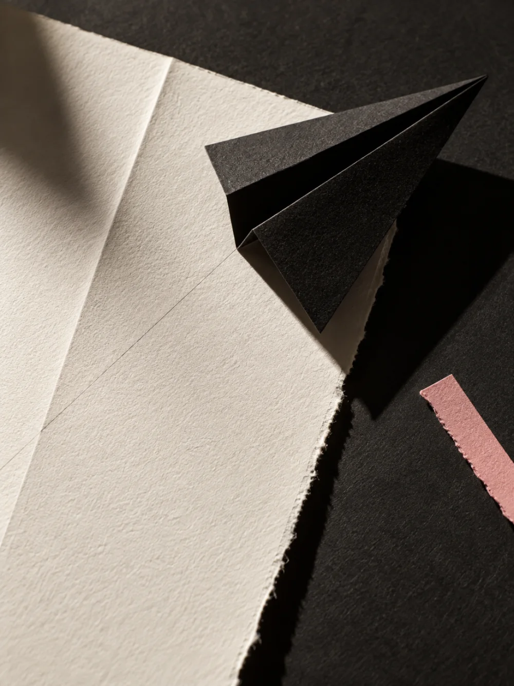 A folded sheet of paper with a sharp black crease and a torn pink strip